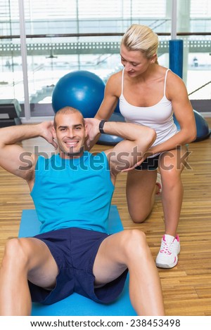 Smiling female trainer assisting young man with abdominal crunches at fitness studio