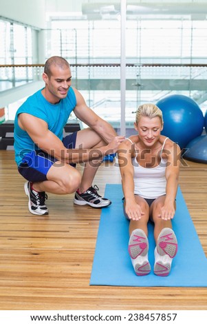 Male trainer assisting young woman with exercises at fitness studio