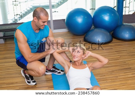 Male trainer assisting young woman with abdominal crunches at fitness studio