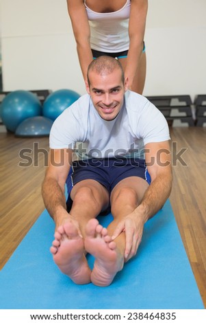 Female trainer assisting young man with stretching exercises at fitness studio