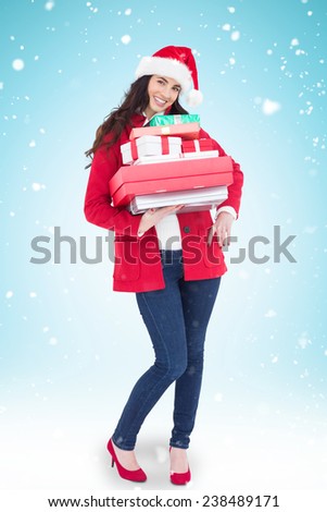 Festive brunette in santa hat and red coat holding pile of gifts against blue background with vignette
