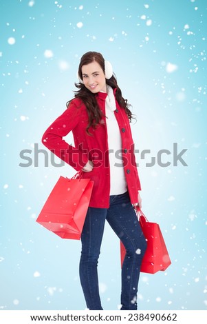 Cheerful brunette in winter clothes posing and holding shopping bags against blue background with vignette