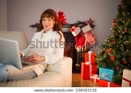 Smiling redhead woman using laptop on couch at christmas Smiling redhead woman using laptop on couch at christmas at home in the living room