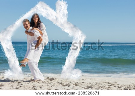 Smiling woman sitting on mans back and looking at camera against house outline in clouds