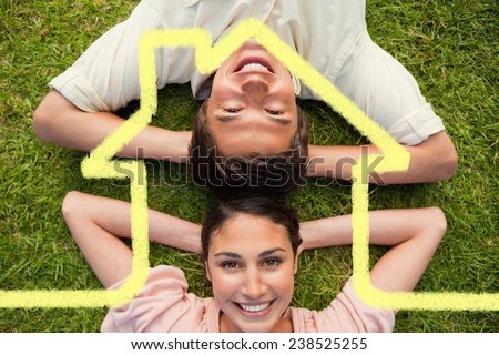 Two friends smiling while lying head to head with both hands behind their neck against house outline
