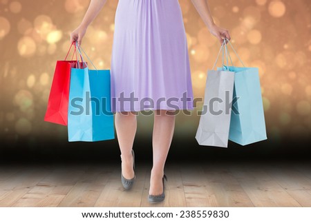 Mid section of woman holding shopping bags against shimmering light design over boards