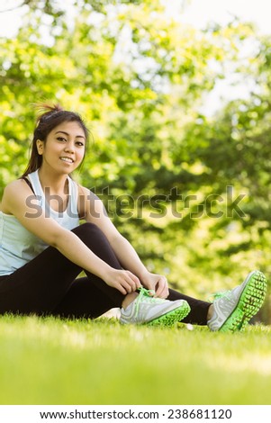 Full length of healthy young woman relaxing in park as she ties shoelace