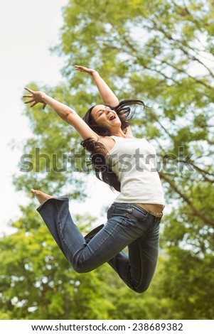 Excited brunette jumping in the park on a sunny day