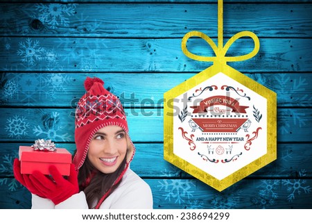 Happy brown hair holding red gift against christmas decorations over wood