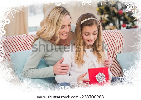 Daughter opening christmas gift with mother against frost frame