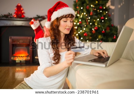 Red hair in santa hat shopping online with laptop at home in the living room