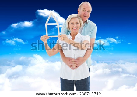 Happy older couple holding house shape against bright blue sky with clouds