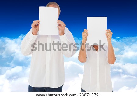 Couple holding paper over their faces against bright blue sky over clouds