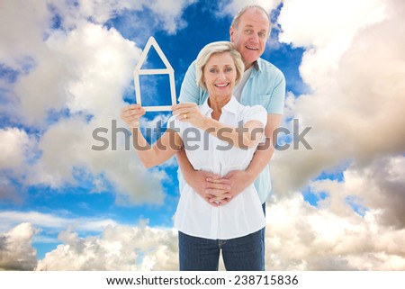 Happy older couple holding house shape against blue sky with white clouds