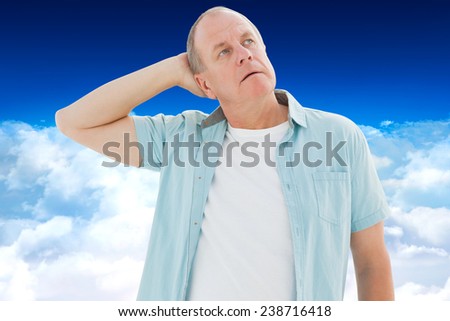 Thoughtful older man looking up against bright blue sky over clouds