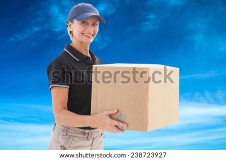 Happy delivery woman holding cardboard box against blue sky