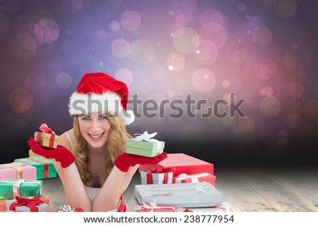 Woman in santa hat laying on the floor while holding gifts against shimmering light design over boards