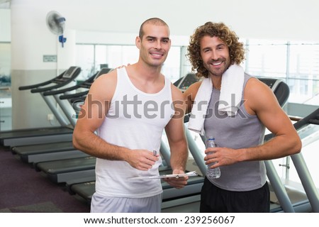Portrait of a smiling male trainer and fit young man at the gym