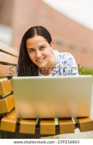 Casual brunette lying on bench using laptop in the park