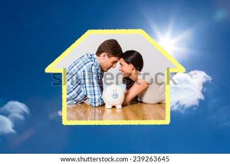 Young couple lying on floor smiling with piggy bank against bright blue sky with clouds