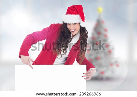 Festive brunette pointing white poster against blurry christmas tree in room