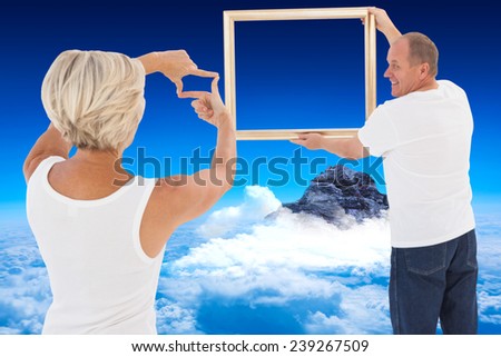 Mature couple hanging up picture frame against mountain peak through the clouds