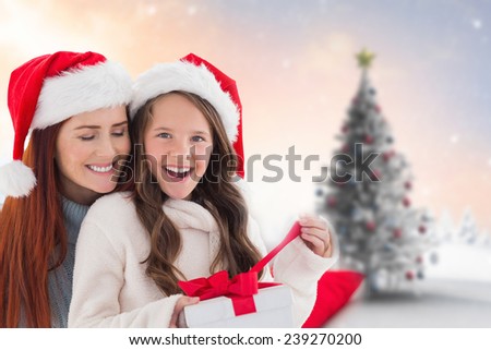 Mother and daughter opening gift against blurry christmas scene