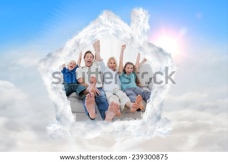 Family sitting on a couch and raising arms against blue sky with white clouds
