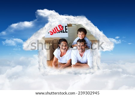 Family in their new house lying on floor with boxes against bright blue sky with clouds