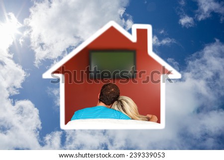 Couple sitting on couch watching a television at home against bright blue sky with clouds