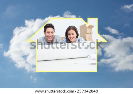Couple lying on the floor and holding a house plan against cloudy sky