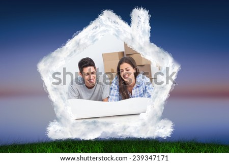 Couple lying on the floor and looking at house plans against green grass under blue and purple sky