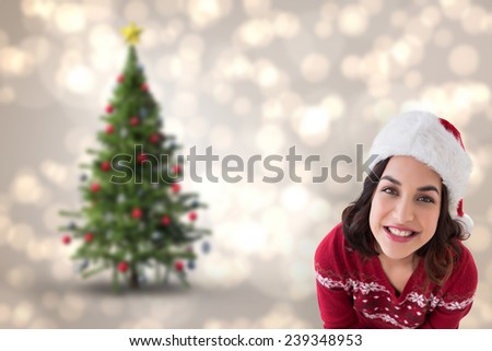 Happy brunette sitting and wrapping christmas presents against blurred christmas tree background