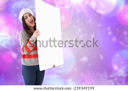 Excited brunette in santa hat showing white poster against blurred lights