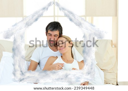 Positive couple drinking coffee lying in the bed against house outline in clouds