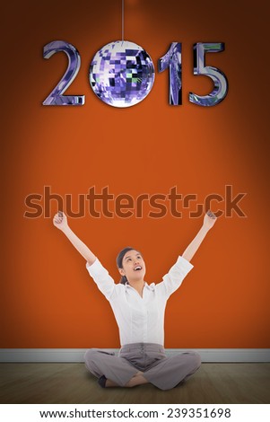 Cheering businesswoman sitting cross legged against room with wooden floor