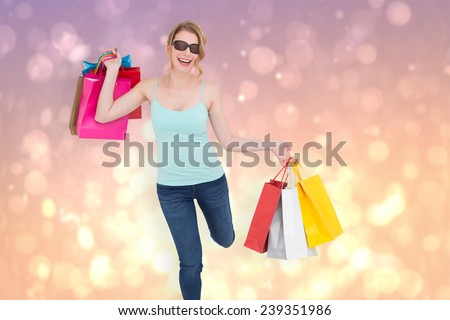Happy blonde holding shopping bags against pink abstract light spot design