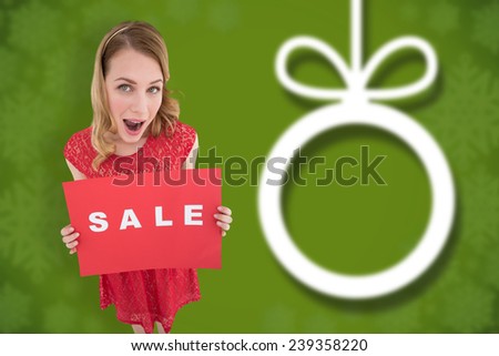 Surprised blonde showing a red sale poster against blurred christmas background