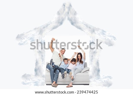 Family sitting on sofa raising their arms against house outline in clouds
