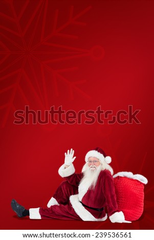 Santa sits leaned on his bag and waves against red background