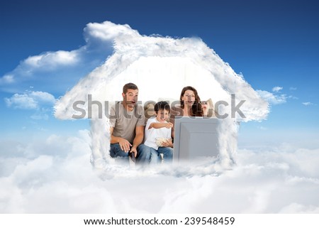 Happy family watching a movie on television together on the sofa against bright blue sky with clouds