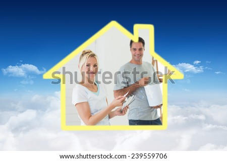 Couple with color swatches and ladder in a new house against bright blue sky over clouds