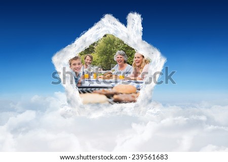 Laughing family having a barbecue in the park together against blue sky over clouds