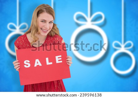 Smiling blonde showing a red sale poster against blurred christmas background