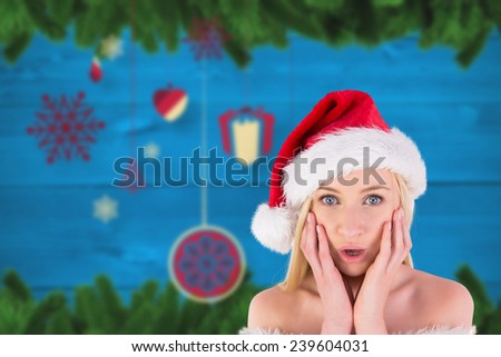 Festive blonde looking surprised with hands on face against blurred fir tree branches on wood