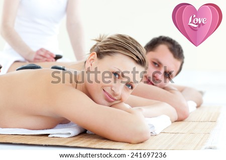 Smiling young couple having a stone massage against love heart