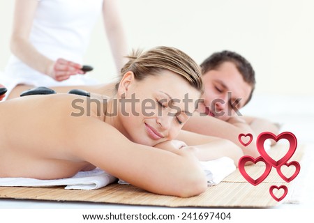 Young couple having a massage with hot stone against pink hearts