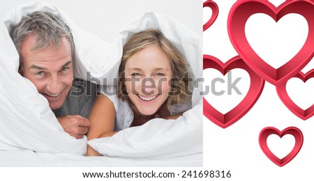 Happy middle aged couple under the duvet against pink hearts