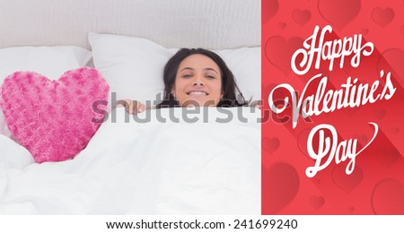 Woman lying in bed next to a fluffy heart pillow against cute valentines message