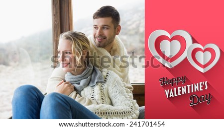 Couple in winter wear looking out through cabin window against happy valentines day